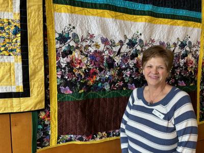 Image of staff in front of a hanging quilt